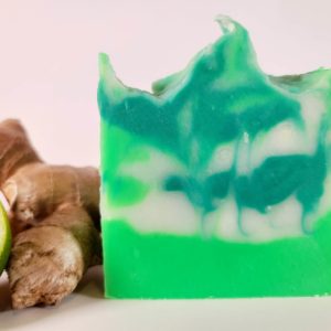 A picture of a green and white swirled soap next to ginger root and a cut lime.