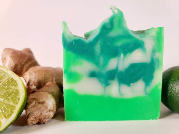 A picture of a green and white swirled soap next to ginger root and a cut lime.