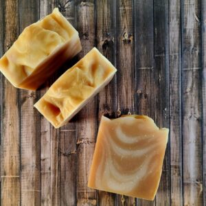 Three tan bars of soap with a creamy swirl sit on a wooden table.