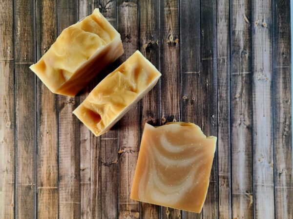 Three tan bars of soap with a creamy swirl sit on a wooden table.