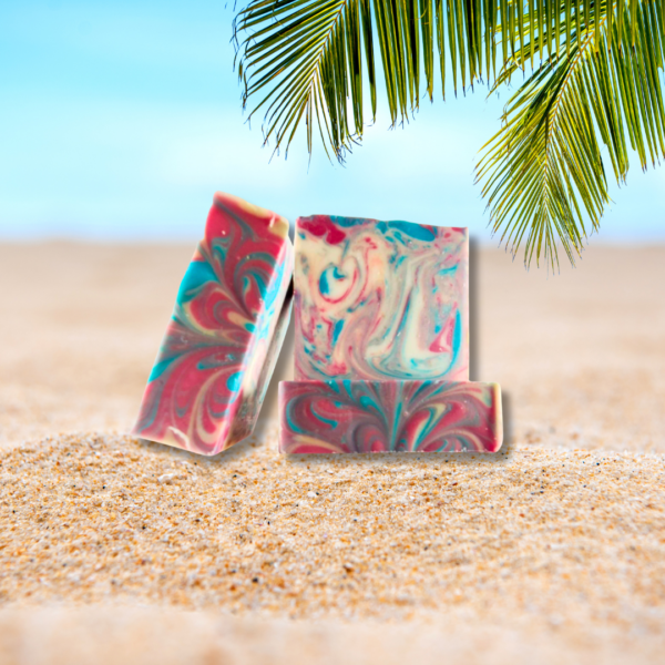 Three green, red, blue, and cream color swirled soaps on a beach with a palm tree frond.