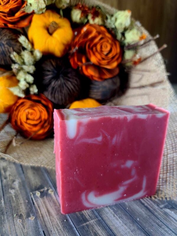 A red and white swirled bar of soap set in front of an arrangement of brown, red, and yellow Fall flowers.