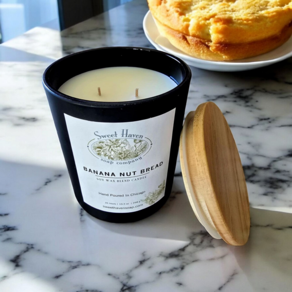 A classy matte black jar holding a white wax candle on a marble table with some banana nut bread in the background.