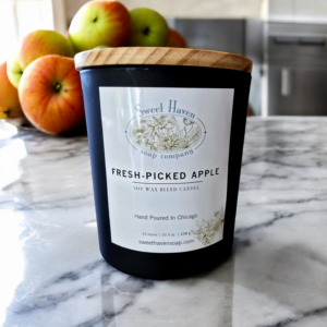 A classy black mat jar containing a soy wax candle sitting atop a white marble countertop with apples in the background!