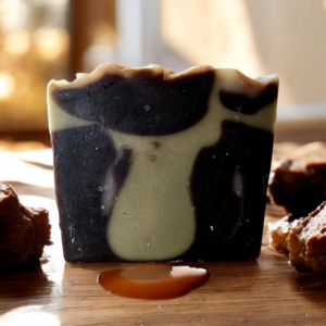 A brown and tan swirled bar soap on a wooden table surrounded by caramel chocolates