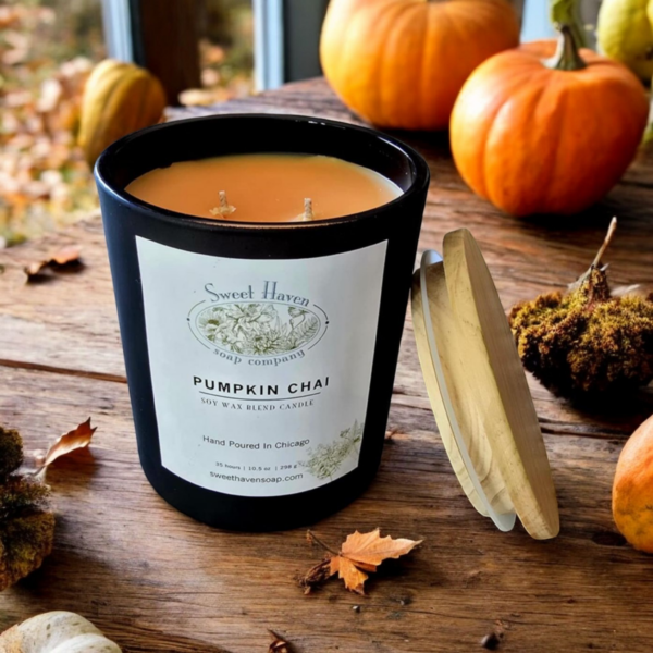 A classy matte black jar with wooden lid leaning on it, sitting atop a wooden table surrounded by pumpkins and leaves.