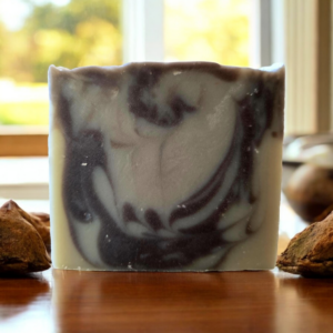 A brown and tan swirled soap sitting on a teakwoood table surrounded by cardamom.