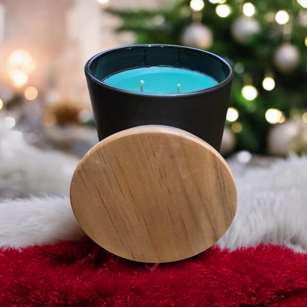 A blue-green colored candle in a black container sitting in front of a Christmas Tree