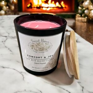 A single Christmas candle, dyed red, with a black container sitting on a marble table in a living room decorated for the holidays. A fireplace is in the background.