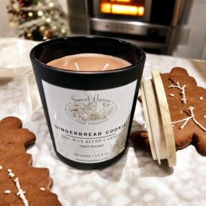 A candle in a matte-black jar sitting on a kitchen counter surrounded by gingerbread cookies