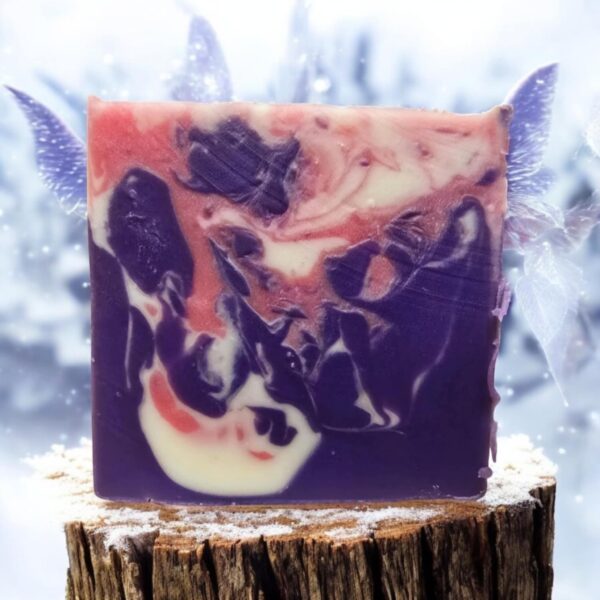 A purple, white, and pink swirled soap on a log outside in the winter.