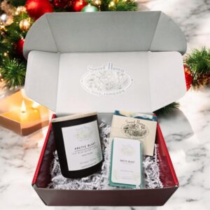 A red gift box with one green-colored candle in a black glass container, one blue, gold, and white swirl4d soap, and one package of green-colored wax melts!